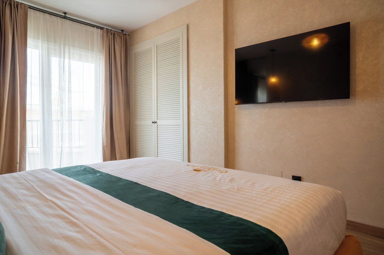 A hotel room with a bed, a television mounted on the wall, and a window with curtains.