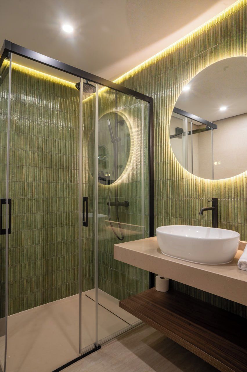A modern bathroom with a glass-enclosed shower, a round mirror, and a white sink.