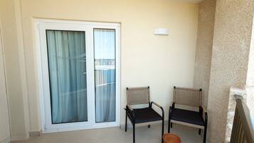 Un balcon avec deux fauteuils en osier, un petit tabouret en osier et une porte-fenêtre à glissière avec des rideaux.