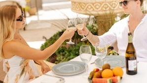 Un espacio de comedor al aire libre con una mesa preparada para dos personas, un frutero y una botella de vino.
