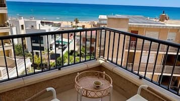 Ein Balkon mit zwei Korbstühlen und einem kleinen runden Tisch, mit Blick auf Strand und Stadtbild.