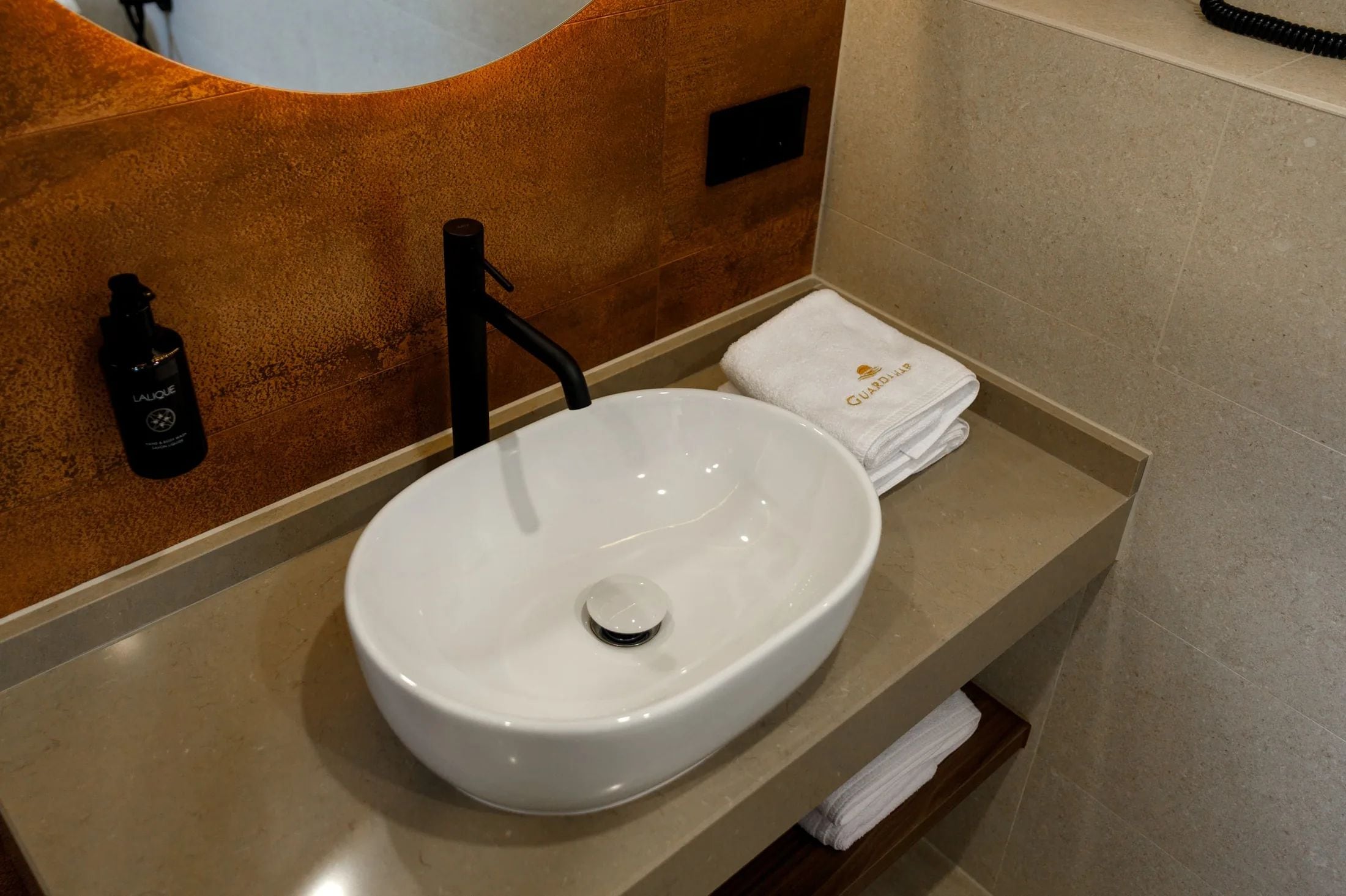 A bathroom with a white sink, a black faucet, a bottle of lotion, and a folded towel.