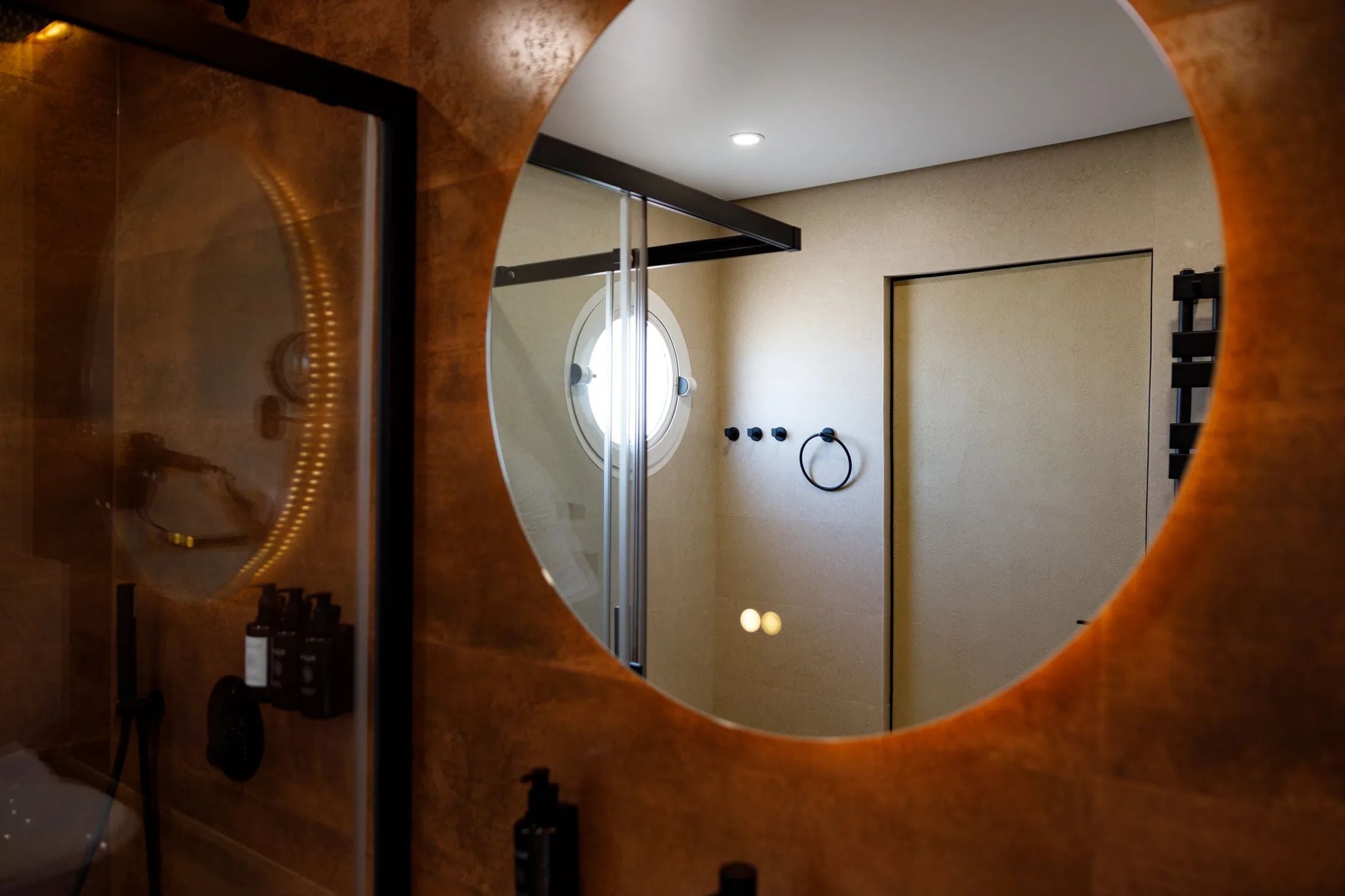 A bathroom with a circular mirror, a shower, and a toilet.