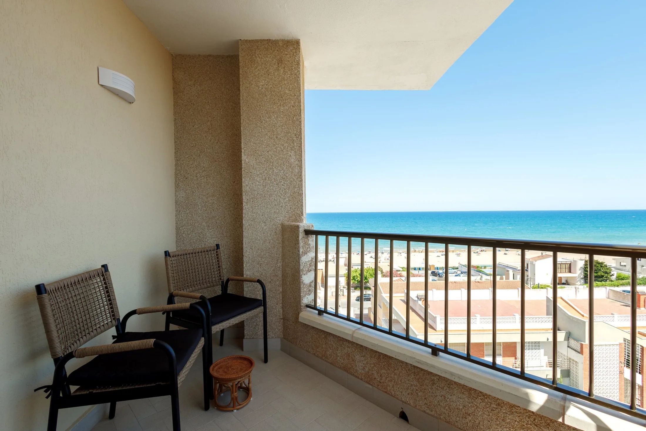 Un balcon avec deux fauteuils en osier et un petit tabouret en fibres tressées.