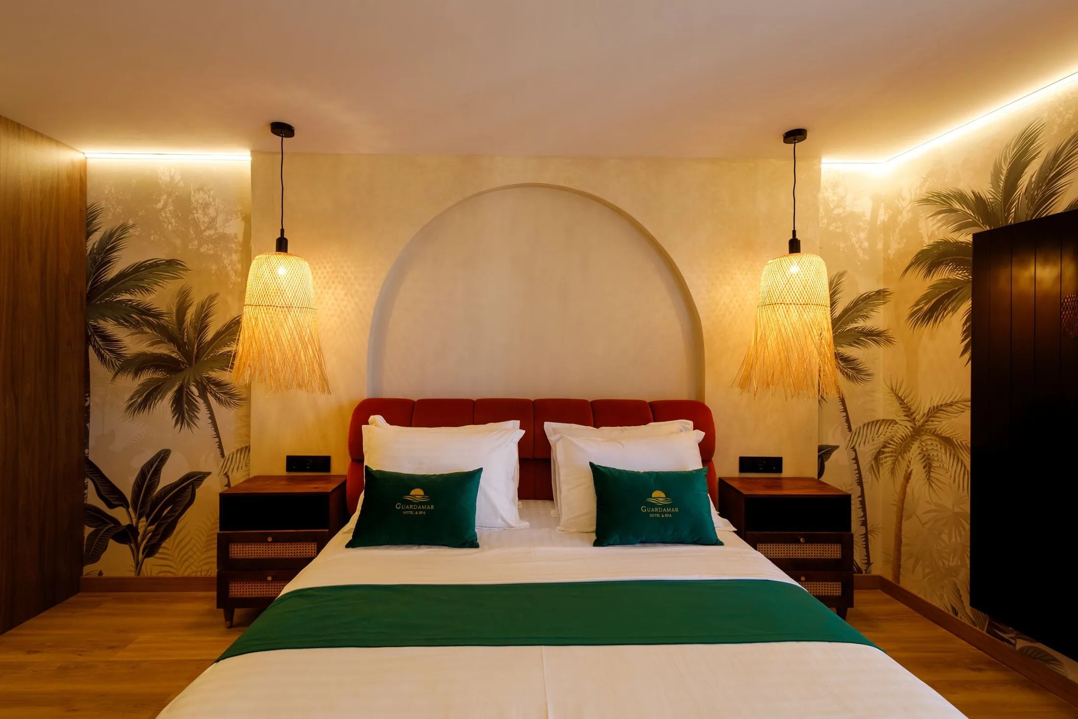 A hotel room with a bed, two nightstands, a red headboard, and wall-mounted lamps.