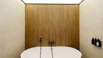 Een moderne badkamer met een vrijstaand bad, een wandpaneel van hout en een handdroger aan de muur.