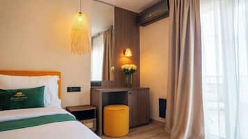 Una habitación de hotel con una cama, una mesita de noche, un taburete pequeño, un espejo, una lámpara en la pared y una ventana con cortinas.