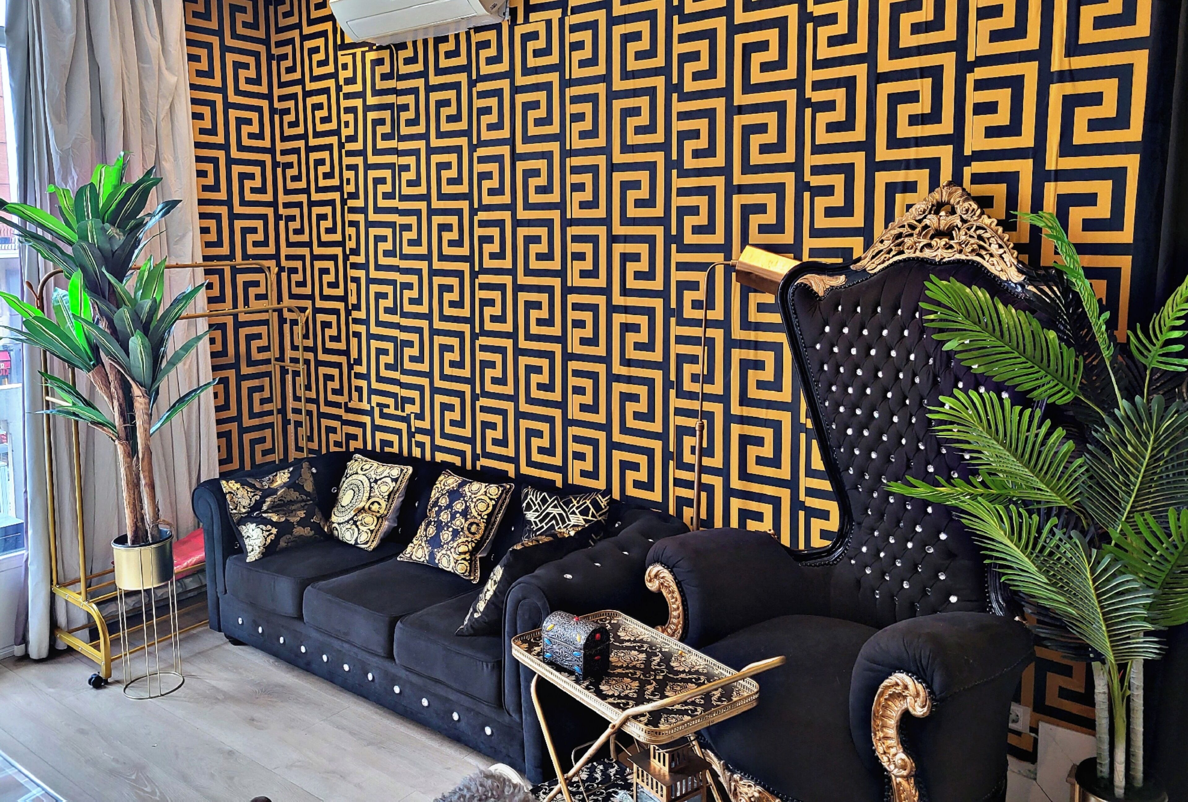 Un salon moderne avec un mur à motifs, un canapé foncé agrémenté de coussins décoratifs, une petite table d’appoint et une grande plante en pot.