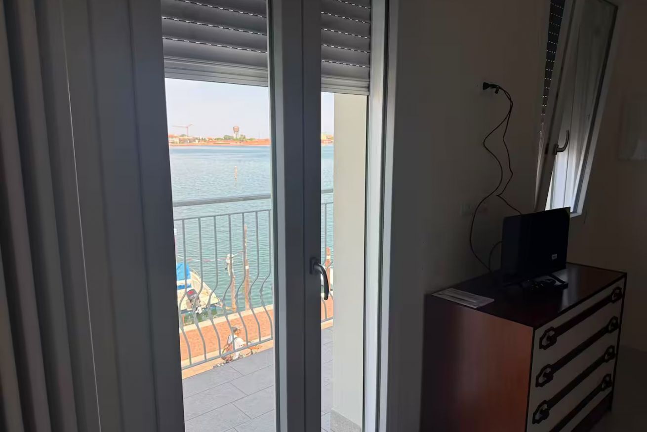 Ein Zimmer mit Blick auf ein Gewässer, ein Balkon mit Geländer und eine Holzkommode mit Schubladen.