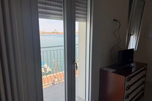 A room with a view of a body of water, a balcony with a railing, and a wooden dresser with drawers. - Bella Laguna | Veranda with lagoon views and private kitchen (Chioggia)