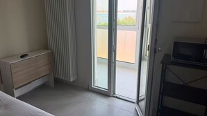 Una habitación con puerta corredera de vidrio que da a un balcón, un pequeño armario de madera y un televisor sobre un soporte.