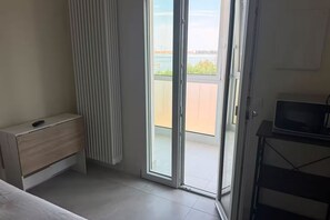 Ein Zimmer mit einer Schiebeglasdoor zu einem Balkon, einem kleinen Holzschrank und einem Fernseher auf einem Tisch.