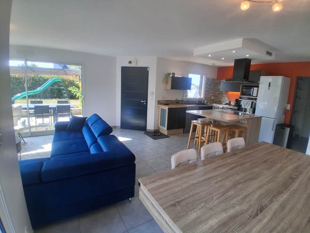 A modern interior with a blue sofa, a wooden dining table, and a kitchen area.