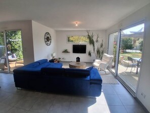 Un salon moderne avec un canapé d’angle, un téléviseur à écran plat et une grande porte-fenêtre coulissante donnant sur un espace extérieur.