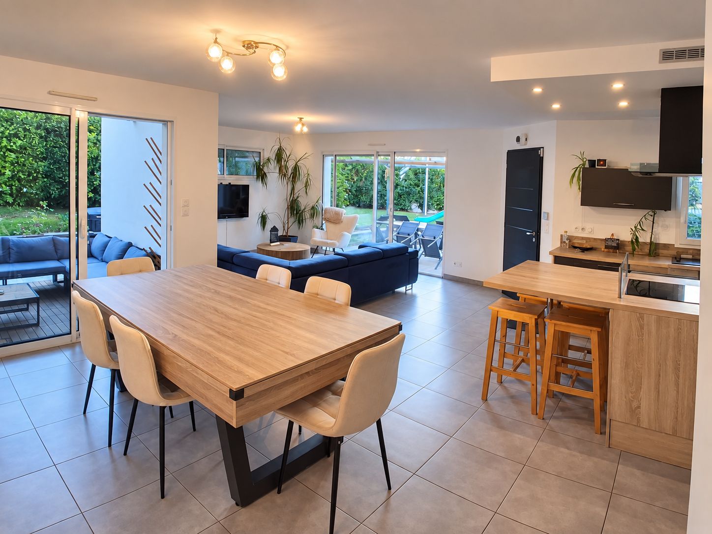 Eine moderne Küche mit Essbereich, einem Fernseher und einer Glastür, die auf eine Terrasse führt.