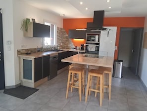 Une cuisine moderne dotée d’un îlot central, d’appareils électroménagers intégrés et d’un mur d’accent d’un orange vif.