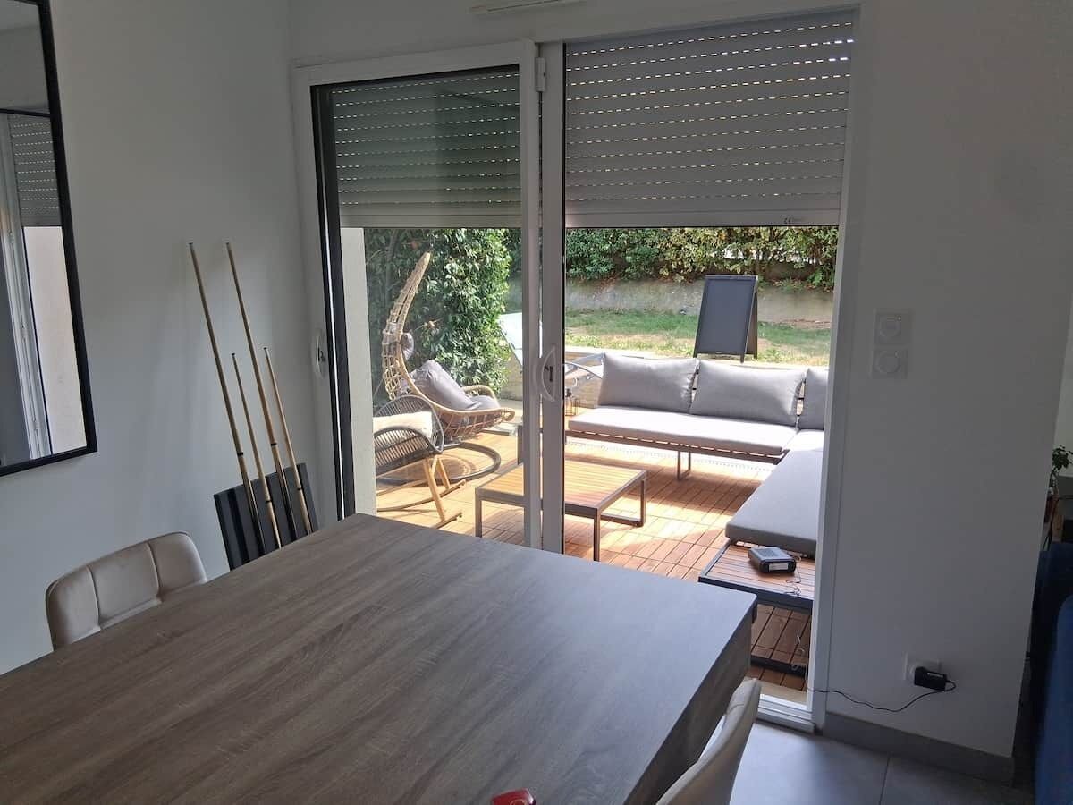 A modern dining area with a wooden table and chairs, a sliding glass door leading to an outdoor seating area with a sofa and chairs.