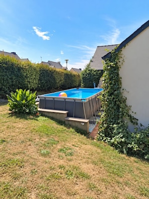 Ein rechteckiger Swimmingpool mit blauer Innenseite, umgeben von einer Rasenfläche und einem Heckenstreifen.