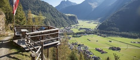 A mountain overlook with a wooden deck, a flag, and a view of a valley with houses and fields.