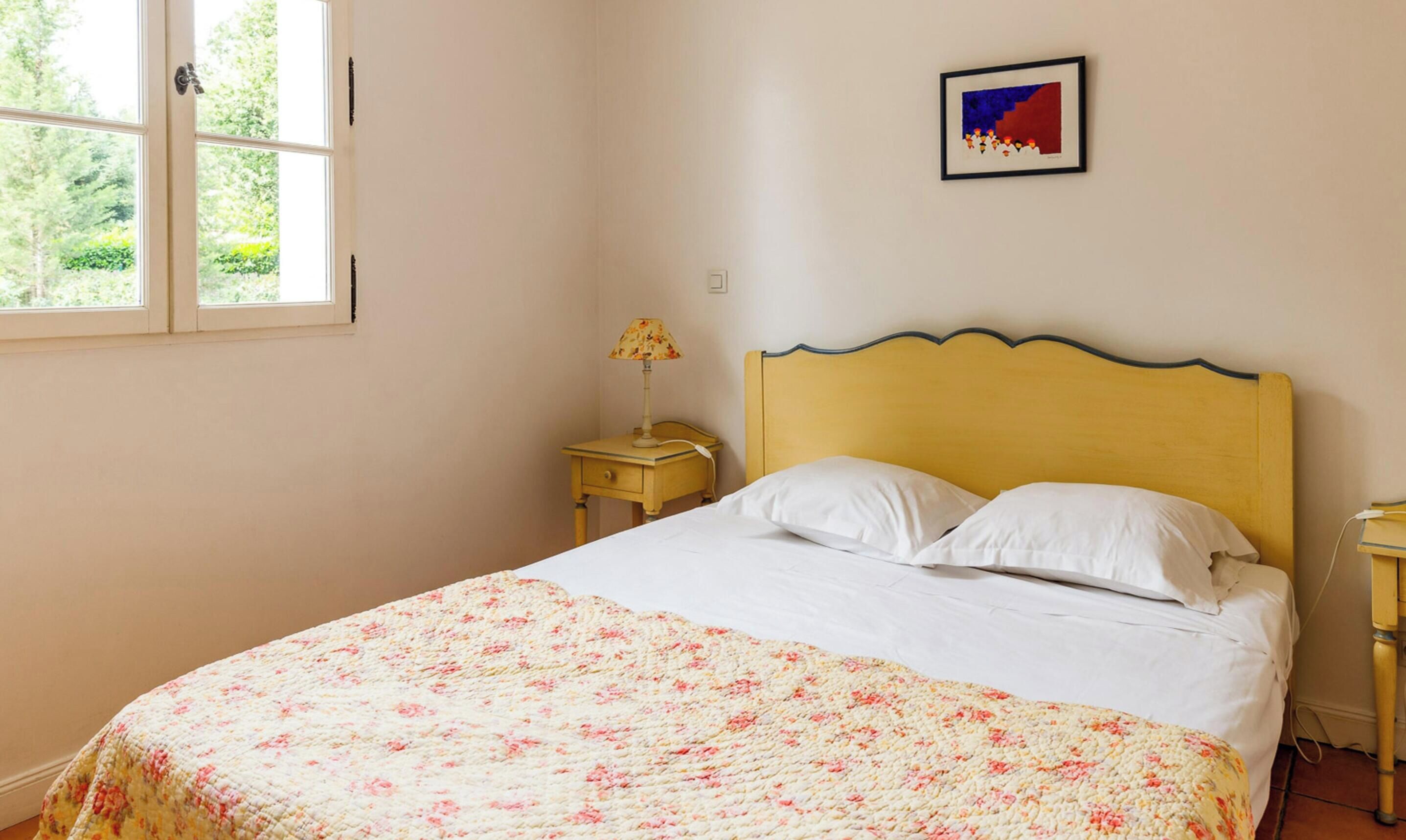 Una habitación con una cama, una mesita de noche, una lámpara y un cuadro enmarcado en la pared.