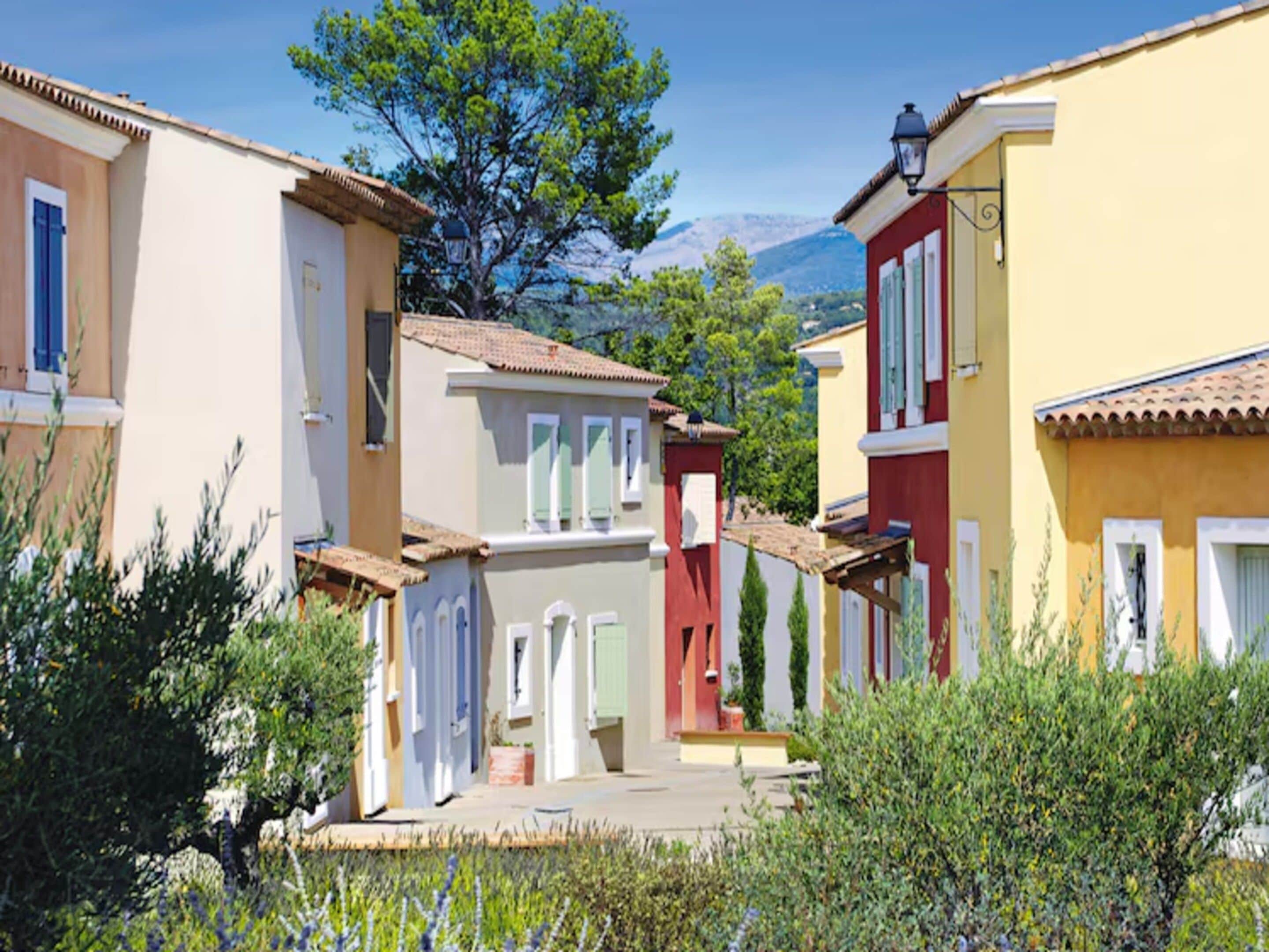 A narrow street with buildings on either side, a tree in the center, and a mountain in the background.