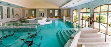 Una piscina interior con varias pistas de natación, un jacuzzi central y una escalera que lleva a un balcón con vistas.
