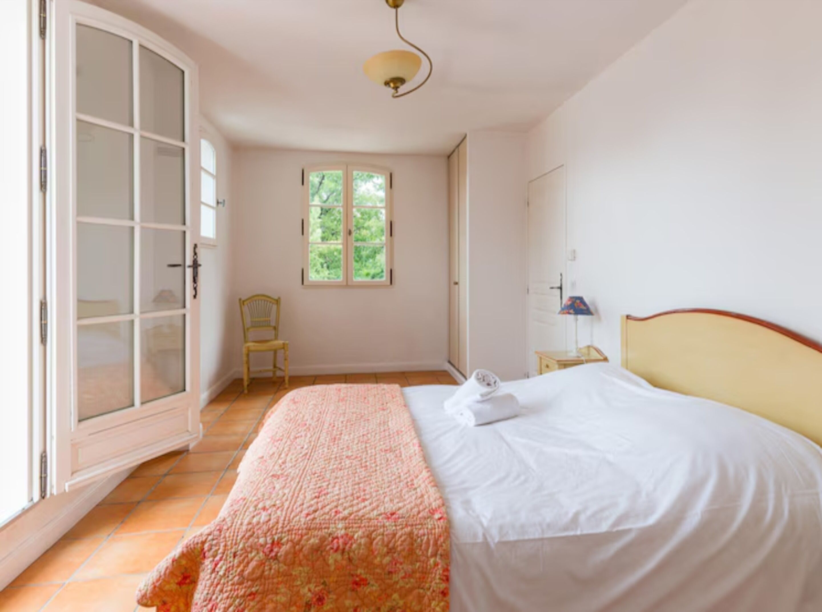 Un dormitorio con cama, una silla, un ventanal y una puerta.