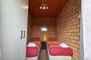 Ein Zimmer mit zwei Betten, einem kleinen Fenster und einer Holzbalkendecke.