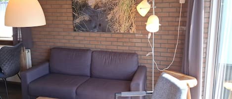 Una habitación con un sofá, una silla, una lámpara y un cuadro en la pared.