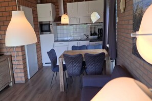 Eine kompakte Küche mit weißen Schränken, einer Mikrowelle und einem Spülbecken. Es gibt einen Essbereich mit einem Holztisch und vier Stühlen.