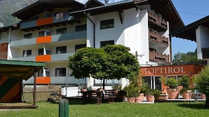 Un hôtel à plusieurs étages doté de balcons, une enseigne indiquant « TOPTIROL », et un arbre au premier plan.