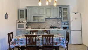 A kitchen with a dining table set for four, a refrigerator, and a clock on the wall. - Il Casale Di Brunella (MONOPOLI)