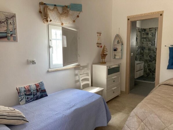Un dormitorio con cama, cómoda, silla y espejo, además de un baño con ducha.
