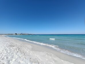 Una spiaggia con acqua cristallina, sabbia bianca e una montagna in lontananza.