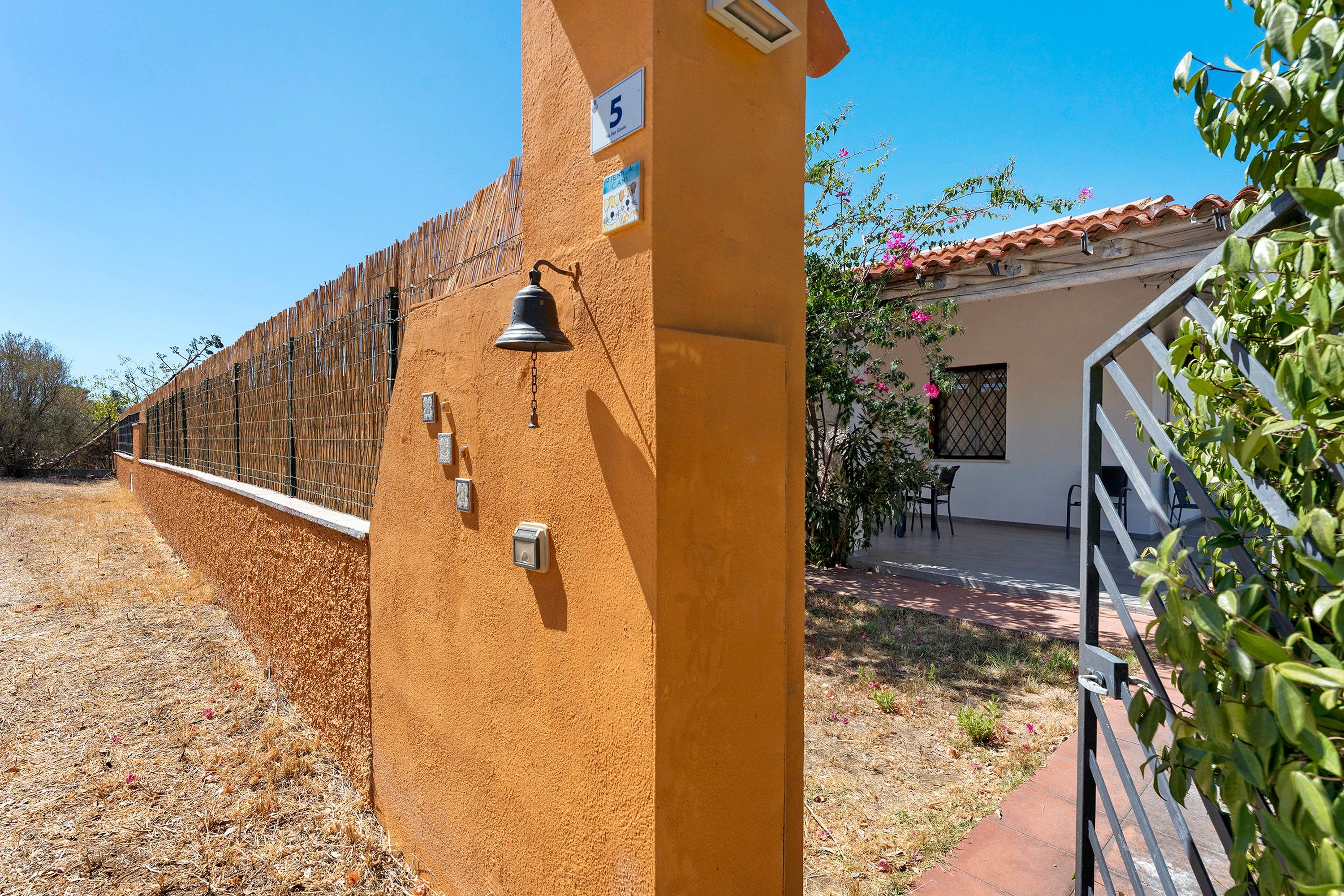 A yellow wall with a number sign, a bell, and a small window.