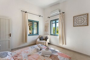 Un dormitorio con cama, dos ventanas con cortinas, un equipo de aire acondicionado, un adorno en la pared y una puerta.