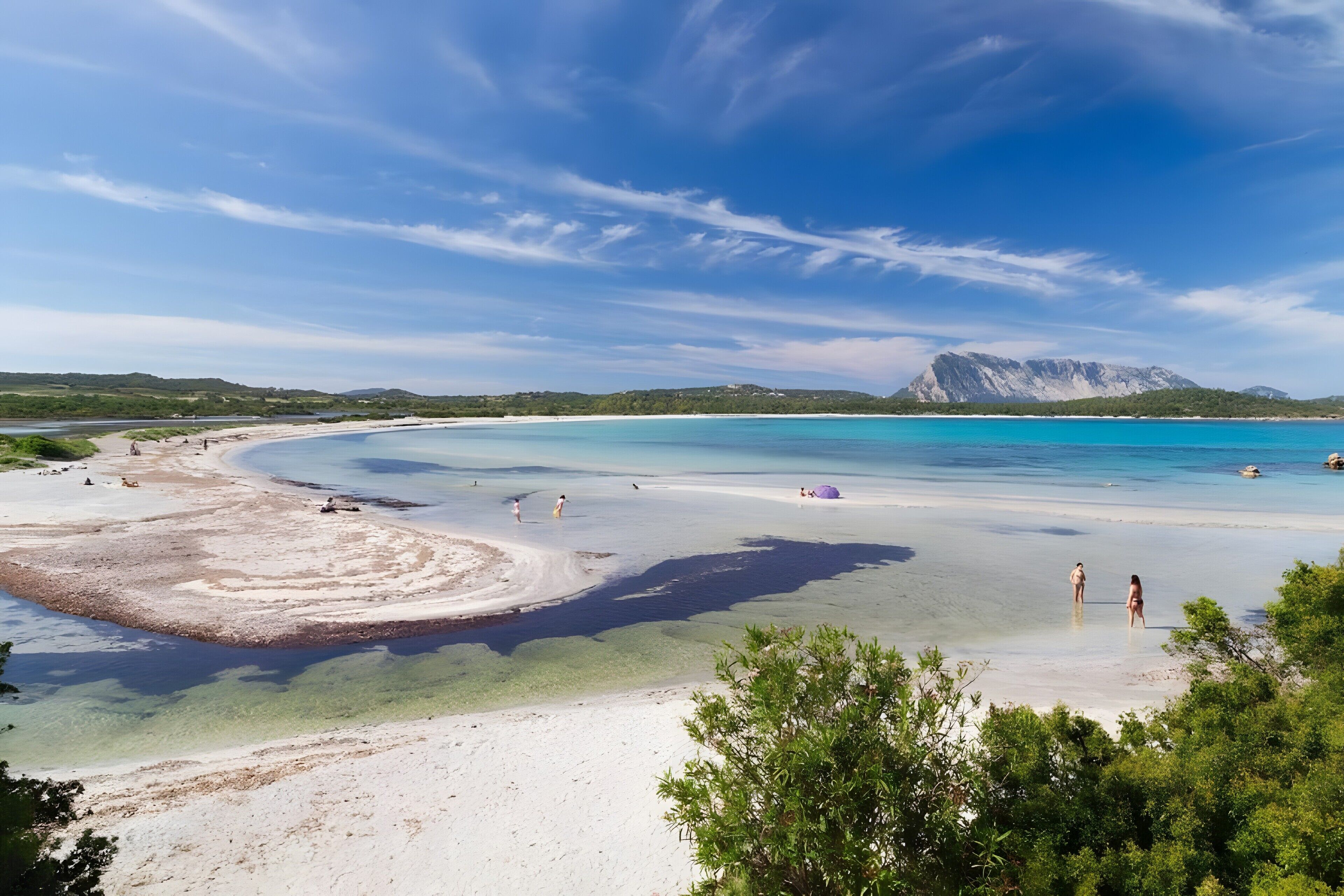 Un paisaje costero con aguas transparentes, una playa de arena y una montaña al fondo.