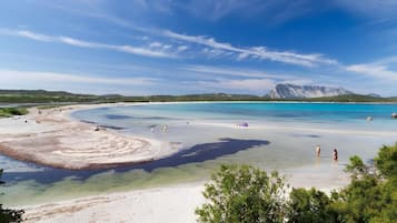 Un paisaje costero con aguas transparentes, una playa de arena y una montaña al fondo.