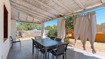 Un patio techado al aire libre con una mesa y sillas, techo de madera y vista del jardín circundante.
