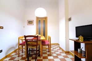 A room with a checkered floor, a wooden dining table with chairs, a television on a stand, and a door with a mirror. - Boccaccio Boutique Apartment (Firenze)
