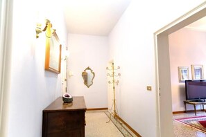 A hallway with a wooden dresser, a mirror, a coat rack, and a television in the background. - Boccaccio Boutique Apartment (Firenze)