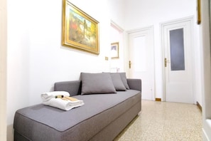 A room with a grey sofa, a painting on the wall, and a door with a frosted glass panel. - Boccaccio Boutique Apartment (Firenze)