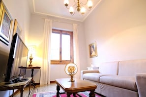 Une pièce comprenant une télévision, une lampe, un canapé, une table agrémentée d’un objet décoratif et une fenêtre avec des rideaux.