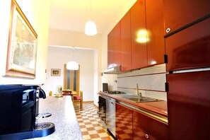 Une cuisine compacte équipée d’un four à micro-ondes, d’une cuisinière et d’un évier. Le sol est carrelé et un tableau encadré orne le mur.