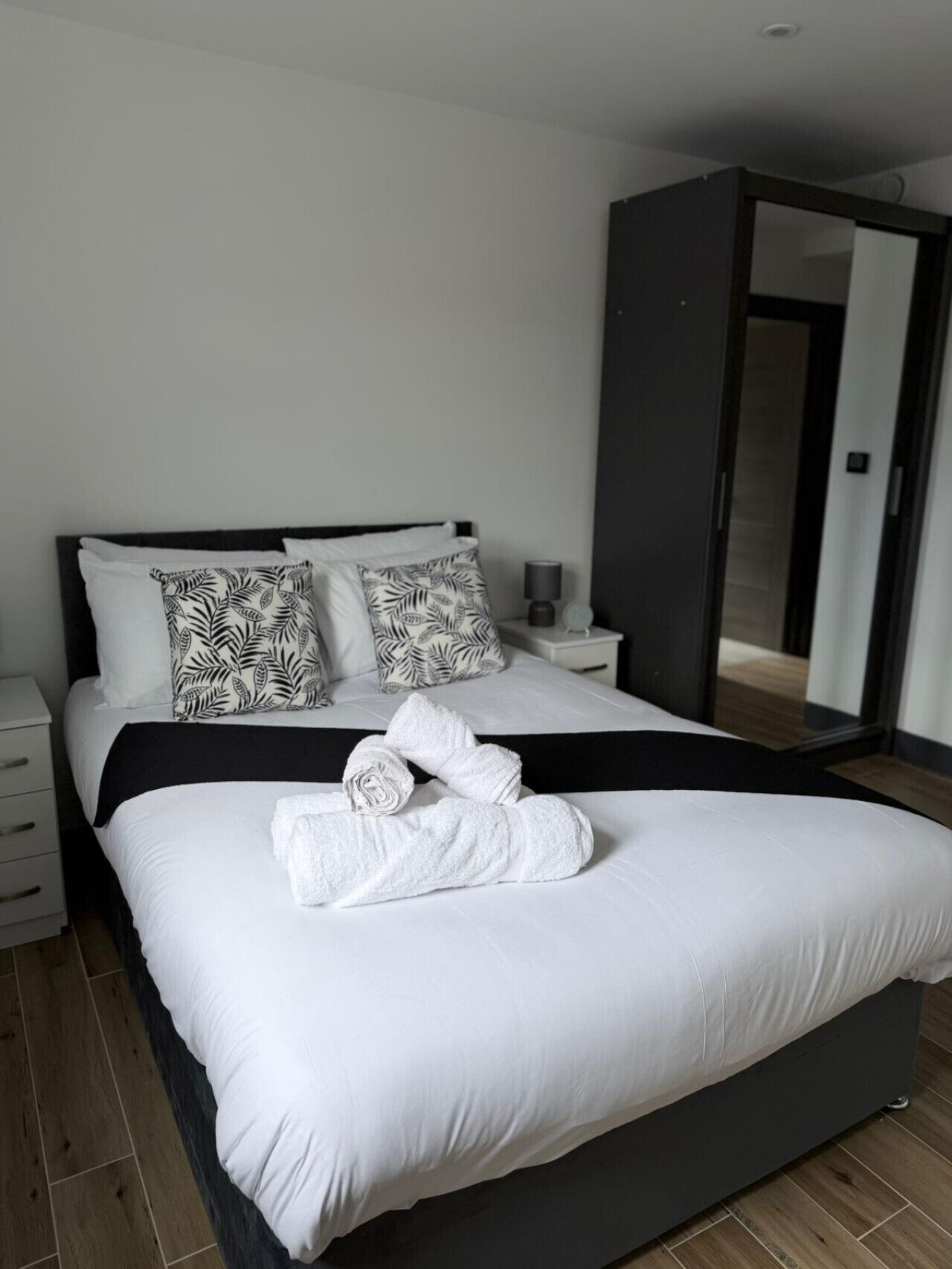 Ein modernes Schlafzimmer mit einem großen Bett, zwei Nachttischen und einem dunkel gefärbten Kleiderschrank.