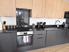A modern kitchen with a black countertop, stainless steel appliances, and wooden cabinets. - Modern 2BR/2BA | Private Balcony & Free Parking (Hertfordshire)