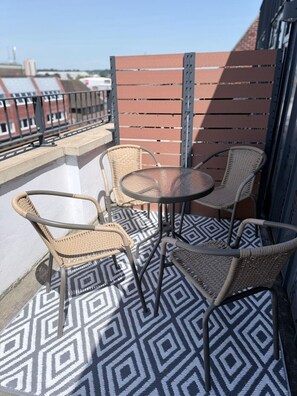 Een balkon met rieten stoelen, een glazen tafel, een patroon vloer en een metalen leuning.