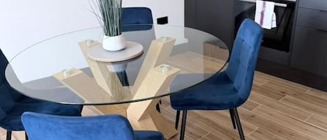 A modern kitchen with a round glass table, blue chairs, and a potted plant.