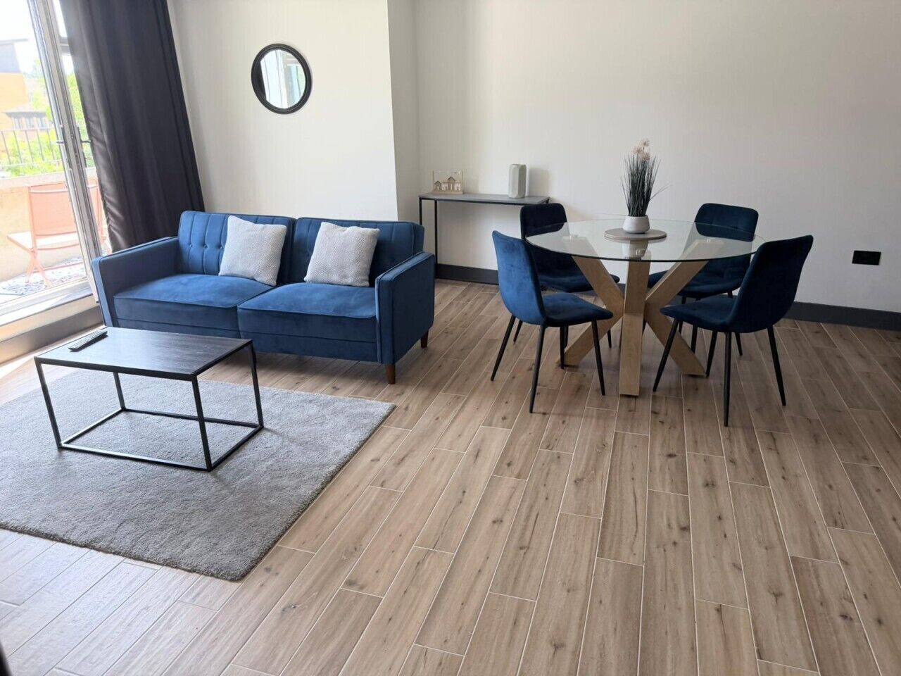 Un salon moderne avec un canapé bleu, une table basse en verre et un coin repas comprenant une table ronde et des chaises.
