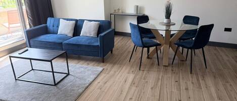 Un salon moderne avec un canapé bleu, une table basse en verre et un coin repas comprenant une table ronde et des chaises.